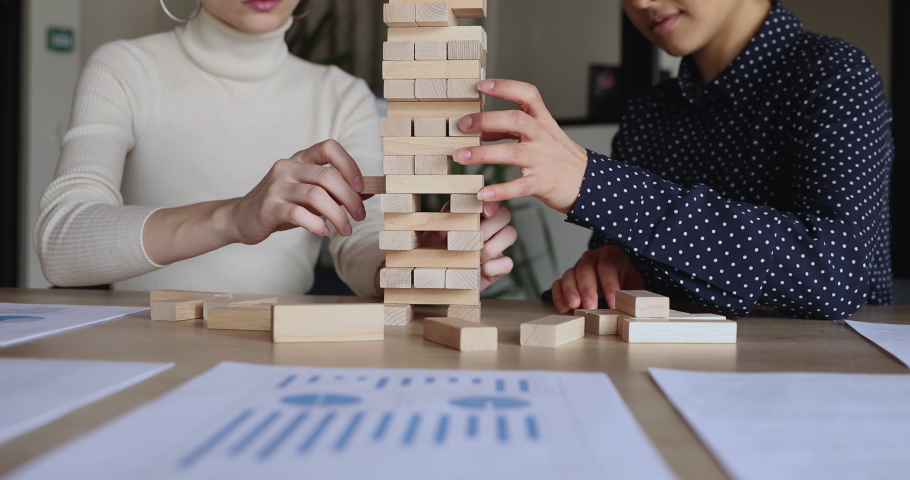 Female partners taking wooden bricks out of tower playing build game on office table. Business insurance, effective risk strategy, building economic stability, credit investment concept. Close up view Royalty-Free Stock Footage #1052489986