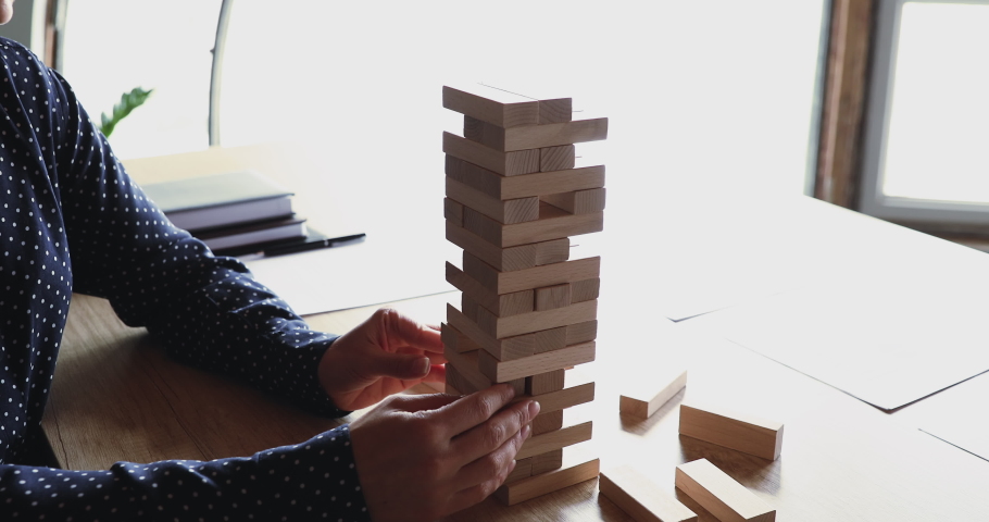 Female hands taking wooden bricks out of tower falling down playing build game on office desk. Bad risk management, choice mistake, wrong decision, business strategy failure concept. Closeup view Royalty-Free Stock Footage #1052489992