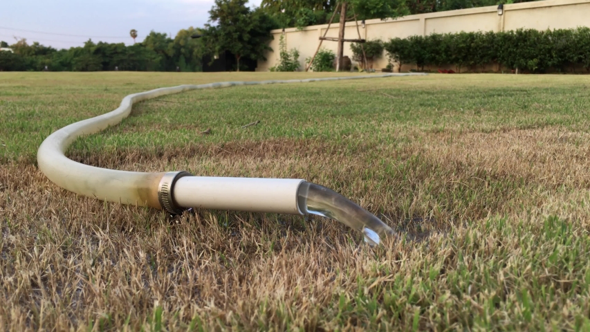Water flows out of the plastic pipe and rubber for watering the grass field with motion gardener pushing the trolley in background