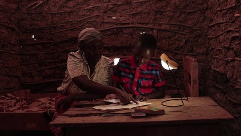 Embu/Kenya 10/‎23/‎2018 : A mother in rural Africa helping his son study under a solar powered lamp. Child and mother in rural Africa using solar lamps.