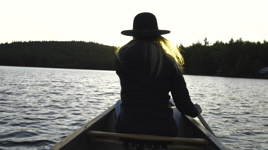 A woman paddles a canoe towards the sunset