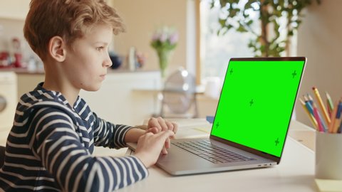 Smart Little Boy Uses Green Screen Chroma Key Laptop for Learning and Video Gaming. Boy Searching for Interesting Information. e-Education, e-Learning, Homeschooling Concept. Over Shoulder