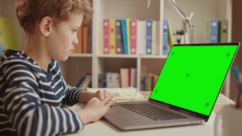 Smart Little Boy Uses Green Screen Laptop for Learning, Writes Down Useful Information. Distance Learning, e-Education, e-Learning Concept