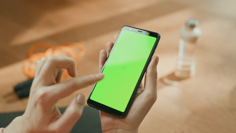 Fitness Concept: Woman Holding Chroma Key Green Screen Smartphone, Does Touch and Click Gesture. In the Background Fitness Mat, Jumping Rope and Equipment. Close-up Point of View POV