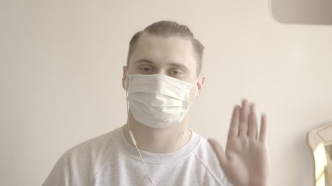 Close-up portrait of young man in face mask greeting colleagues or friends in online chat. Caucasian brunette guy posing for video conference. Covid-19, remote work. 