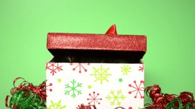 HD video of a Tiny black kitten sitting in a Christmas box surrounded by red and green curly ribbon, green background. Kitten popping in and out of box.
