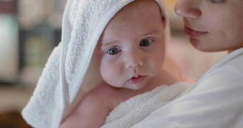 newborn baby in a white towel in her mother’s arms. in slow motion