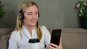 Video of a cute smiling blonde Caucasian girl conducting online communication through the phone with headphones at home.