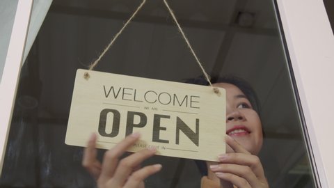 Business owner asian woman turning Welcome we are open sign on fronton glass door store. Reopening activity after COVID-19, ended the lockdown and quarantine. Restarting again and keep forward concept