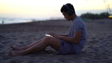 Young man working on modern laptop on the beach