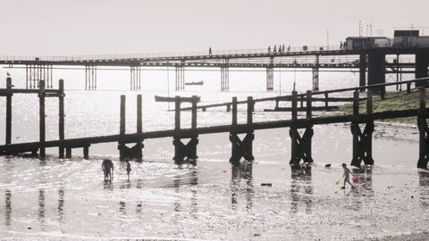 Wooden slipway and pier stretching into the sea over the beach. Children are playing on the sand with a family