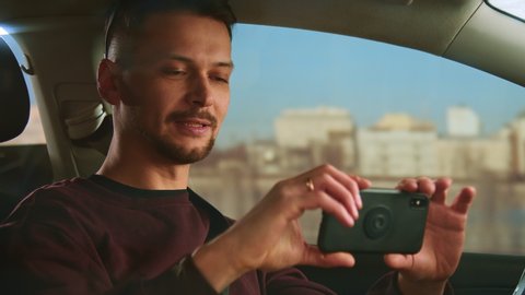An attractive man drives a car and shoots a video blog on a smartphone.