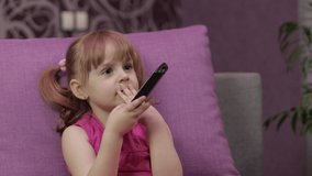 Cute little kid sitting on the couch while watching TV at home in the evening. Beautiful young child daughter girl watch television on living room. Concept video game, entertainment, family, relax