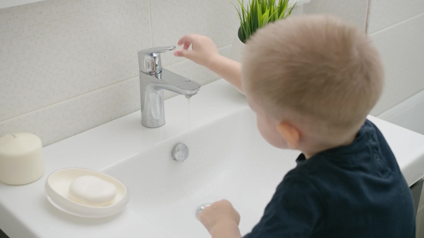 A small child learns to open a tap with water and wash his hands Royalty-Free Stock Footage #1052530595