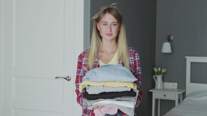 Young housewife holding clean clothes and looking at camera