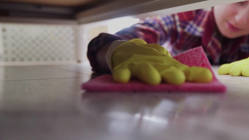 Close up of woman cleans the floor under bed with special detergent.