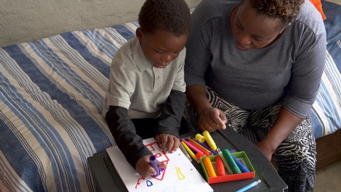 Black African woman home schooling her cute young little boy at home during lockdown for Covid-19 Coronavirus pandemic, South Africa