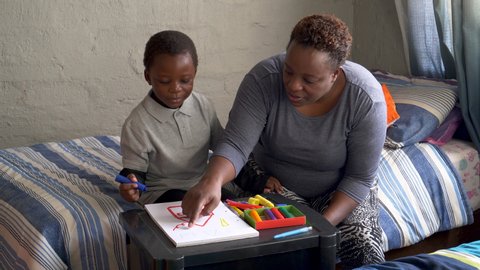 Poverty.Inequality.Black African woman home schooling her cute young little boy at home during lockdown for Covid-19 Coronavirus pandemic, South Africa