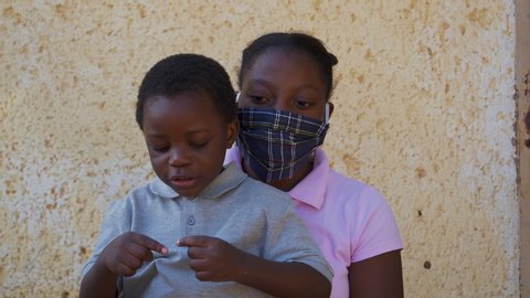 Poverty. Inequality.Young Black African girl puts on a mask on her cute little brother during lockdown to prevent Covid-19 Coronavirus pandemic, South Africa