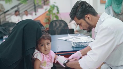 Male nurse finding the vein on a little girl’s arm to insert the cannula at a healthcare facility in Karachi, Pakistan. 20th October 2017