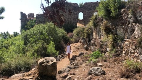 a girl in a white dress walks through the ruins of the Syedra fortress in Alanya, Turkey