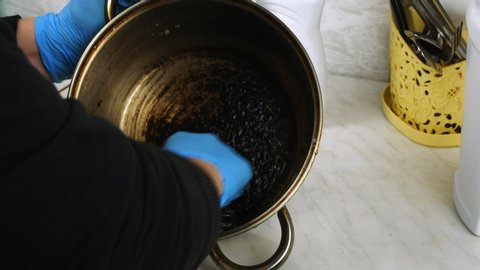 Clean with a wire brush the burnt pan.Cleaning in the home kitchen.Hands removes carbon from the dish.Effective cleanser.Difficult to perform the task.Blue rubber gloves on the palms.