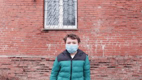 Teenager boy wearing blue protective mask and yellow jacket on street. Quarantine, self isolation, depression, social distance, mental health concept. Stock slow motion video.