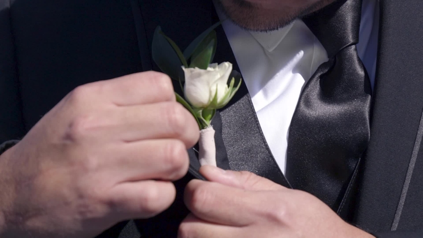 Close up of groom adjusting boutonniere