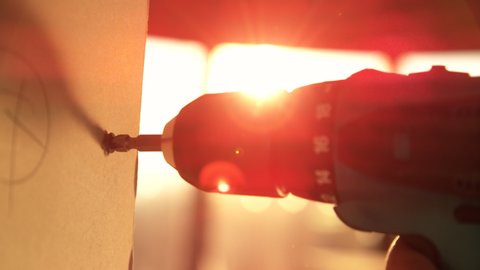 SUPER SLOW MOTION, MACRO, LENS FLARE, DOF: Builder working early uses an electric drill to mount a wall panel on a sunny spring morning. Golden sunbeams shine on power drill fastening a small bolt.