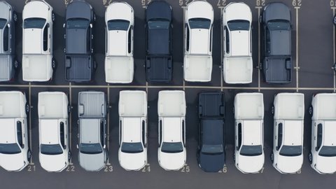 Aerial top down view of the dealership or customs terminal parking lot with a rows of new pickup trucks