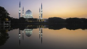 Time lapse of sunrise and scattered clouds by a lake with reflection at Sultan Salahuddin Abdul Aziz Shah Mosque in Selangor, Malaysia. Pan up motion timelapse. Prores Full HD