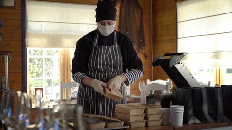 Restaurant worker wearing medical mask and gloves collecting a food box take away. Food delivery services during coronavirus pandemic and social distancing. Online contactless food shopping.