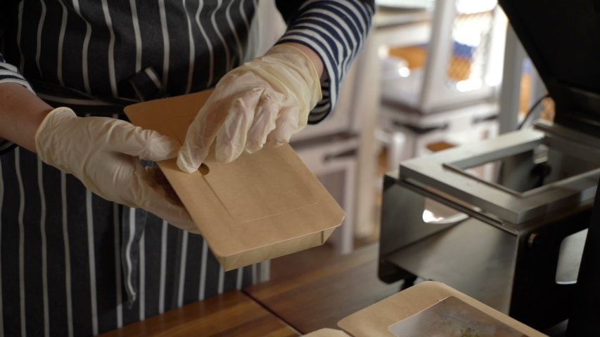 Restaurant worker wearing medical mask and gloves collecting a food box take away. Food delivery services during coronavirus pandemic and social distancing. Online contactless food shopping. Royalty-Free Stock Footage #1052582870