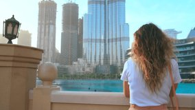 Beauty happy young woman tourist smiling at embankment Dubai. Girl model blonde long loose hair flying in wind. Pink trendy cat sunglasses. Backdrop modern skyscraper building. Blue water UAE 4k 2020