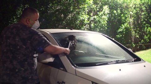 Indian man wiping down his car with a long handled brush to make it ready for the lockdown opening up in India. Shows cars abandoned for months during the coronavius covid 19 lockdown being checked