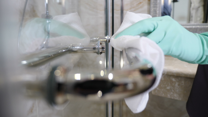 Cleaning chrome-plated bathrooms, bidets. polishing crane and handles. Cleaning in hotel. Close-up shot of maid from hotel staff wiping bath handles, bathtub in toilet at residential building . Shot Royalty-Free Stock Footage #1052592539