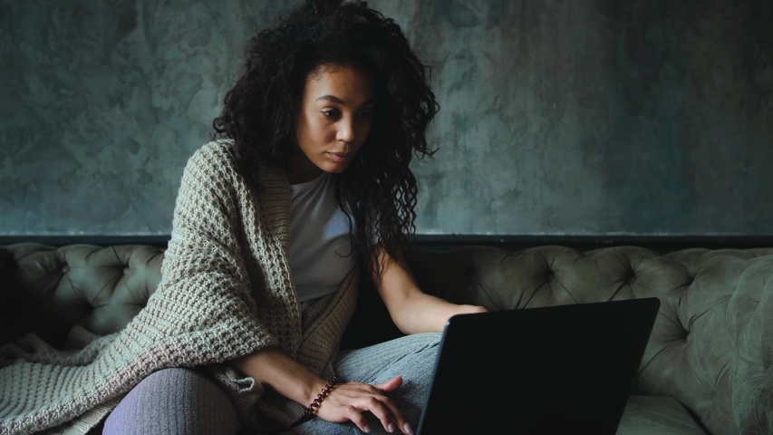 Young african american woman feeling disappointed reading news using laptop at home. Dark cinematic look Royalty-Free Stock Footage #1052595002