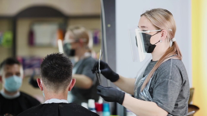  A hairdresser with security measures for Covid-19, cuts hair with a scissors to a man in a medicine mask, social distance, cutting hair with a medical mask, face shield , gloves Royalty-Free Stock Footage #1052596622