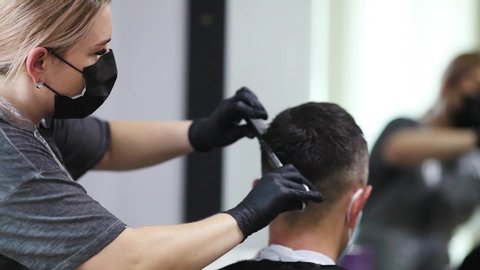 A hairdresser with security measures for Covid-19, cuts a man in a medical mask with a scissor, social distance, cutting hair with a medical mask, a protective mask and rubber gloves in a beauty salon