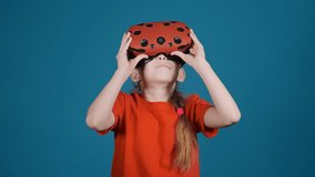 happy little girl with plait in orange t-shirt uses virtual reality headset to play game on blue background slow motion