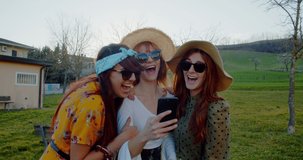 Slow motion 4K video of three beautiful women having fun laughing using smartphone outdoor at summer. Young people generation z and technology concept