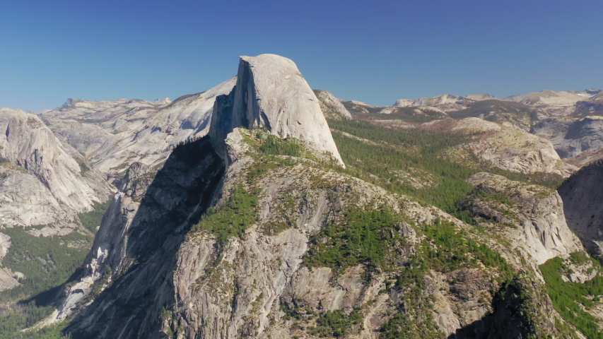 Inspiring aerial panoramic view of large Sierra Nevada massif in Yosemite National Park with its symbol - Half Dome rock in the center of the frame. Picturesque highlands under clear blue sky. 4K
