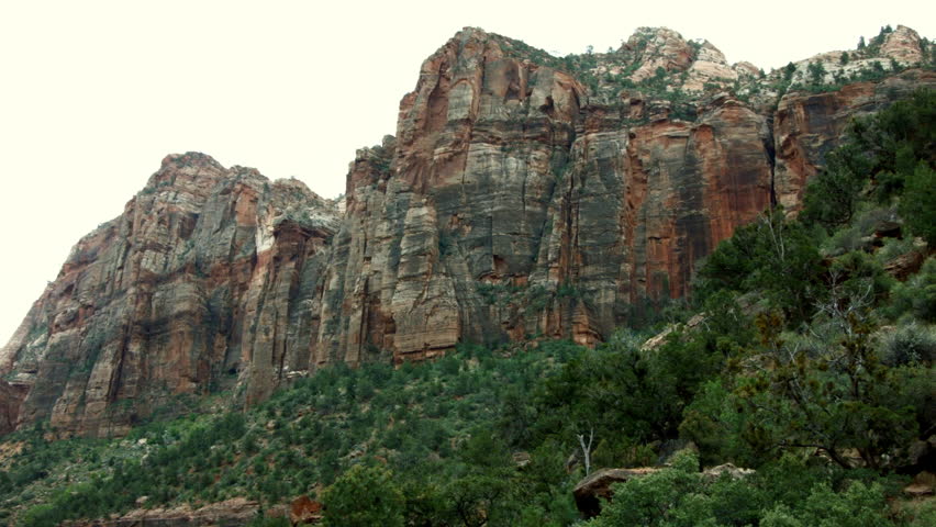 MOUNTAIN CLIFFS TOWER OVER THE VALLEY BELOW.  SLIGHT CAMERA PAN OF THIS COLORFUL MOUNTAIN AND IT