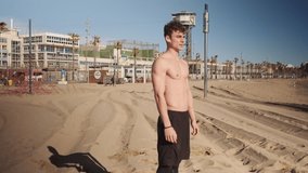 Tracking in shot of attractive fit guy confidently looking in camera after workout on beach