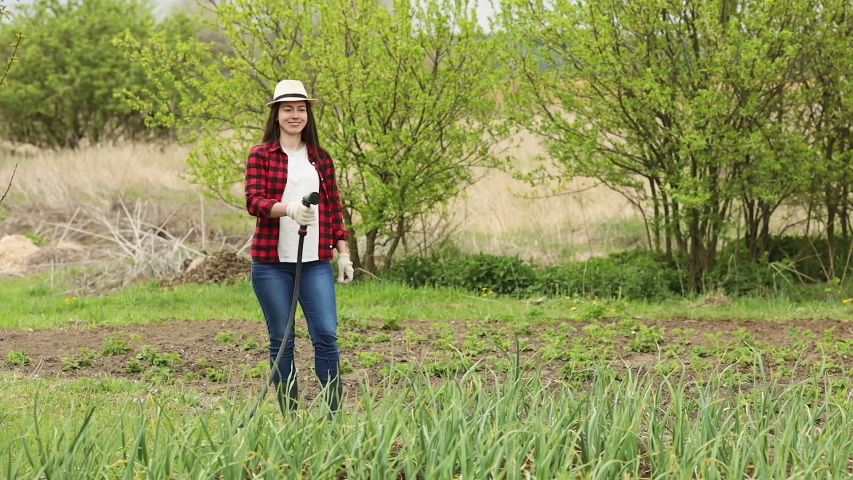 smiling woman gardener watering vegetable garden with hose