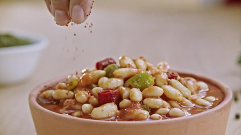 Red pepper powder is thrown on the beans cooked in Turkish style. Slow motion.