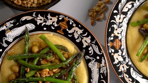 Flat lay closeup of Italian bowls with polenta, chickpeas and asparagus with pine nuts, red wine and lemons.