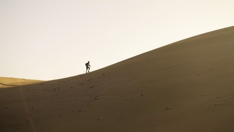Wide Drone Slow Motion Shot Of Man Walking Up Sand Dune In Desert Like Barren Landscape