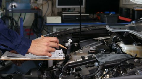 male mechanic checking and repair service a car with clipboard