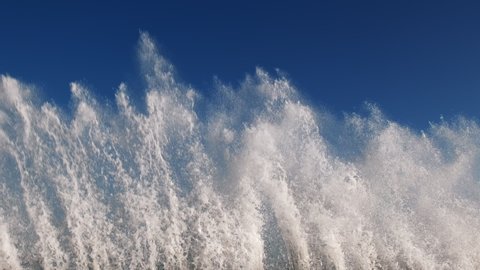 Sea wave with splashes of water and foam slow motion front view on pier against blue sky and forest horizon in storm. Column of water and foam gradually rolls breaking on the stones of pier
